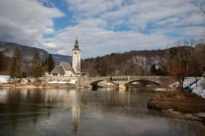 a bridge over a river with a church and a clock tower at Bright loft near Bohinj lake in Bohinj