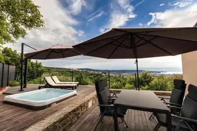 a deck with a hot tub and chairs and an umbrella at Casa Badiha in Zgornje Škofije