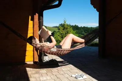 a woman laying in a hammock reading a book at House of Nature Tajhte in Planina pri Sevnici