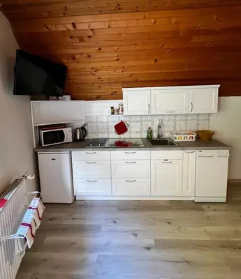 a kitchen with white cabinets and a tv on the wall at Apartma Lip in Rateče