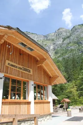 a wooden building with mountains in the background at Planinski dom Savica in Bohinj
