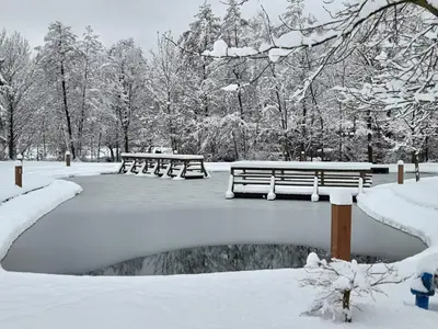 a park covered in snow with benches and a pond at Apartments Kamp Podgrad Vransko in Vransko