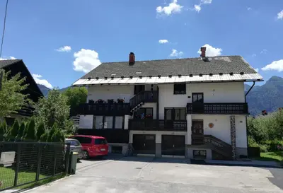 a white house with a balcony and a red van at Apartma Vojvoda in Bohinj