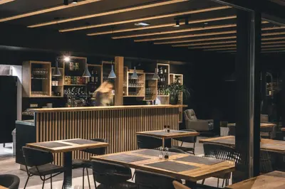 a restaurant with tables and a woman standing behind the counter at Hotel Majerca Superior in Bohinj