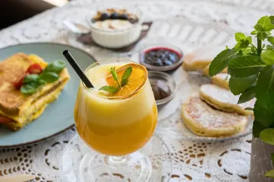 a glass of orange juice on a table with a plate of food at Hiša Poljana Rooms in Prevalje