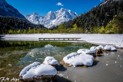 a river with snow covered rocks and mountains in the background at Klass 103 in Kranjska Gora