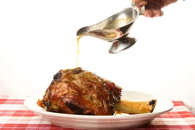 a person is pouring gravy onto a cooked meat at Guesthouse Muha in Lipica