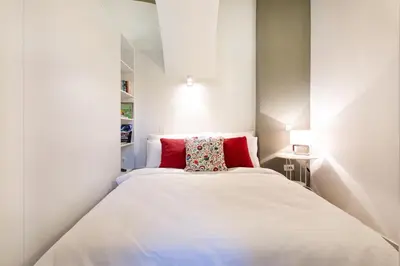 a small bedroom with a white bed with red pillows at Apartments Tivoli in Ljubljana
