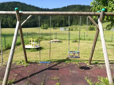 a swing set in a field with a playground at Počitniška hiša Ostrnica in Hrib-Loški Potok