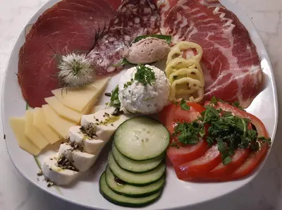 a plate of food with meat cheese and vegetables at SOBE U SIRRC in Bled