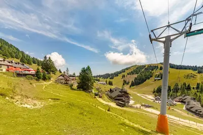 a gondola ride up a green hill with houses at Koča na Krvavcu in Cerklje na Gorenjskem