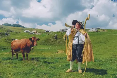 a man is standing next to a cow in a field at Koča Zlatorog - Velika planina in Stahovica