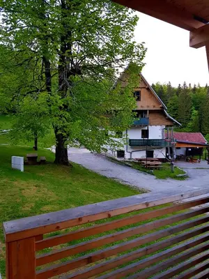 a wooden fence in front of a building with a tree at Planinski Dom na Travni Gori in Sodražica