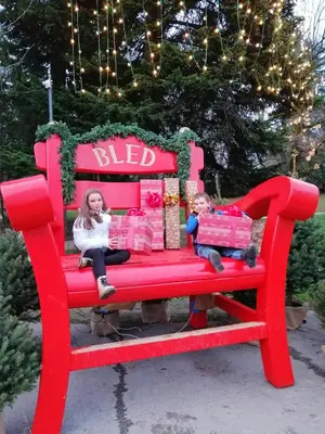a woman and a child sitting on a red bench with gifts at APARTMA CARNICA in Bled