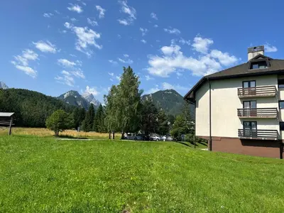 a grassy field next to a building with mountains in the background at Ajda apartment in Kranjska Gora