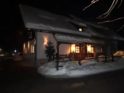 a house with lights on in the snow at night at Apartments Alp in Bohinj
