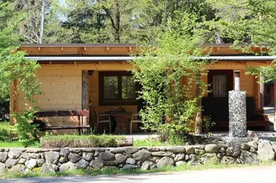 a log cabin with a stone wall in front of it at Wooden lodge with jacuzzi in Rečica ob Savinji