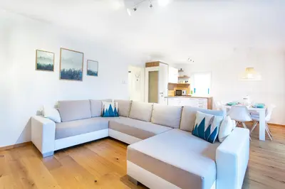 a living room with a white couch and a kitchen at Alpine Home Apartment in Bohinj
