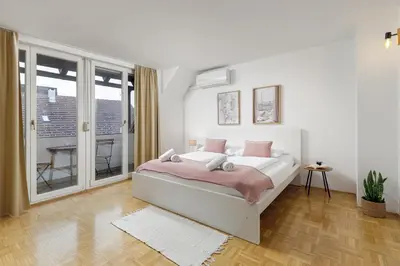 a white bedroom with a bed and a balcony at HoMEMADE in Ljubljana