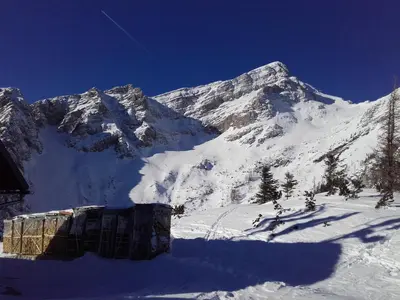 a snow covered mountain with a house in the foreground at Apartma Kramar Podkoren in Kranjska Gora