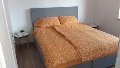 a bed with an orange comforter and two pillows at Apartmaji Pika in Cerklje na Gorenjskem