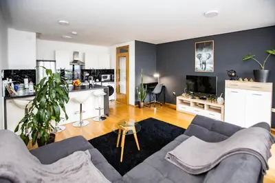 a living room with a gray couch and a kitchen at HERMES APARTMENT & 2 free garage secured parkings in Ljubljana