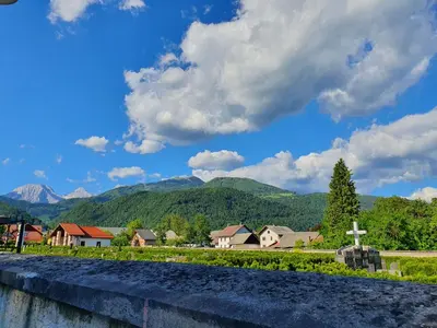 a village with a cross and mountains in the background at Veronica's place in the mountains in Cerklje na Gorenjskem