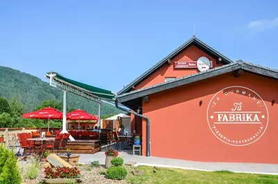 a red building with a restaurant with tables and umbrellas at Ta Fabrika Restavracija,pizzerija in prenočišča in Dravograd