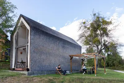a house with a black roof and two people sitting in chairs outside at GORIČKE IŽE in Križevci