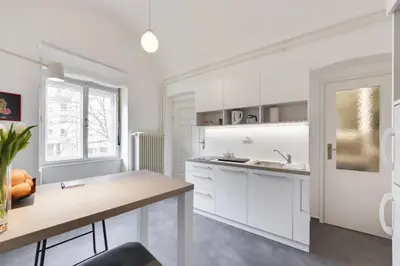 a white kitchen with white cabinets and a table at City Center Apartment with Parking in Ljubljana