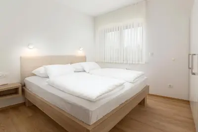 a white bedroom with a large bed with white sheets at Vila Vita Apartments in Kranjska Gora