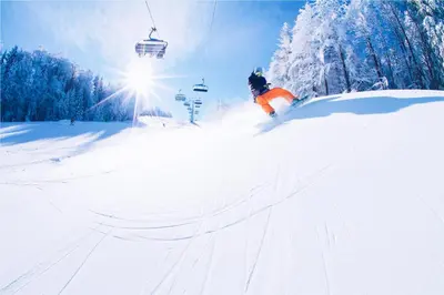 a person skiing down a snow covered slope with a ski lift at Pohorje Village Wellbeing Resort - Family Apartments Bolfenk in Pohorje