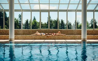 two people laying on the side of a swimming pool at Pohorje Village Wellbeing Resort - Forest Apartments Videc in Pohorje