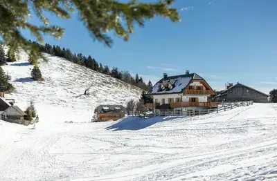 a snow covered hill with a house and two buses at Apartment Jezerca - Krvavec in Cerklje na Gorenjskem