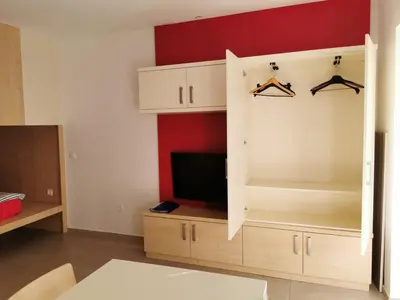 a living room with a tv and a cabinet with hangers at Cube studio by the river (with free bike rental) in Ljubljana