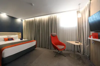 a hotel room with a bed and a red chair at Holiday Inn Express - Ljubljana by IHG in Ljubljana