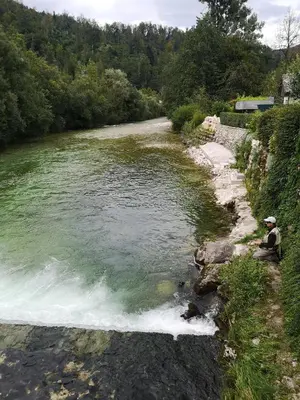 a man sitting on the side of a river at Alpine Joy Apartments in Bohinj