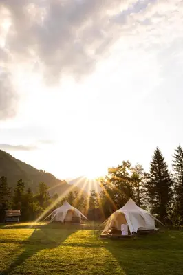 two tents in a field with the sun shining at Glamping Gozdna Jasa in Bovec