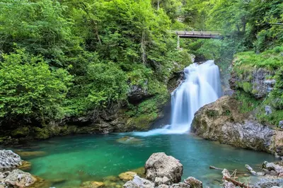 a waterfall in a forest with a bridge above it at Apartments Pr Fajfarju in Bled