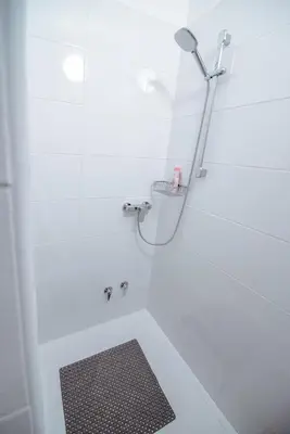 a white bathroom with a shower with a black rug at Apartment Ana - Karst Cycling Paradise in Dutovlje