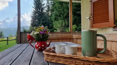 a picnic table with a basket of flowers and mugs at MOUNTAIN ECO CHALET KONJSKA DOLINA on 1400 m asl -near Pokljuka in Srednja Vas v Bohinju