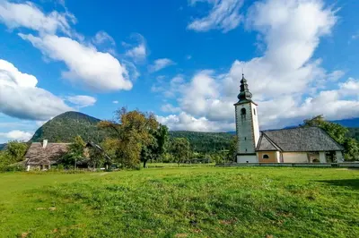 an old church with a tower in a field at Charming blacksmith`s house @ Lake Bohinj in Bohinj