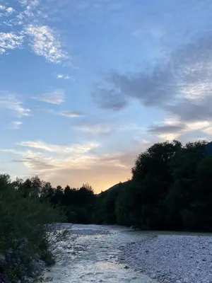 a river with trees and a cloudy sky at Sobe v Gozdu in Gozd Martuljek