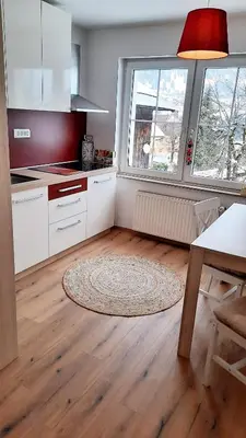 a kitchen with white cabinets and a table and two windows at Apartma Rožle in Mojstrana