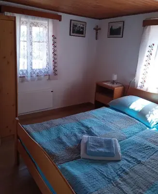 a bedroom with a bed with a blue comforter and two windows at Mountain house MINKA in Srednja Vas v Bohinju