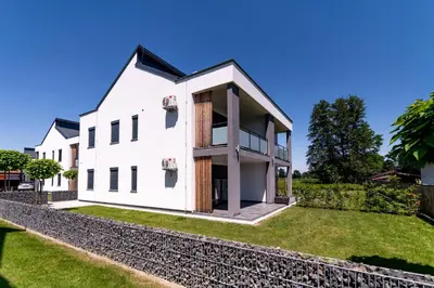 a white house with a stone wall and grass at Apartmaji BANONIA in Veržej