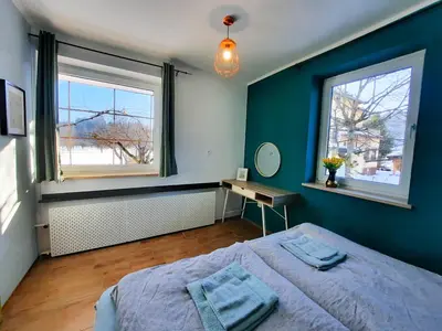 a blue bedroom with a bed and two windows at Deerwood-2-Storey Garden Apartment with Castle view Balcony in Bled