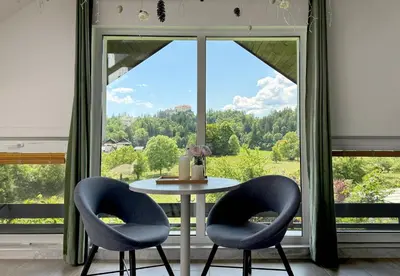 a table with two chairs in front of a large window at Deerwood-Sky Attic with Bled Castle View-NO KITCHEN in Bled