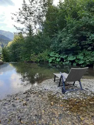 a chair sitting on the beach next to a river at Apartma LUPIS in Podvolovljek