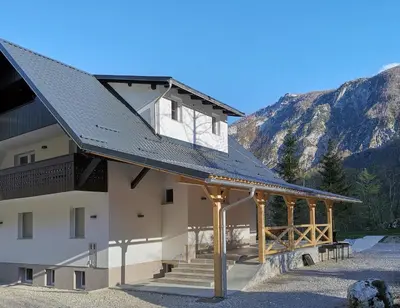 a building with a metal roof with mountains in the background at Holiday House Destina - Lake Bohinj in Bohinj
